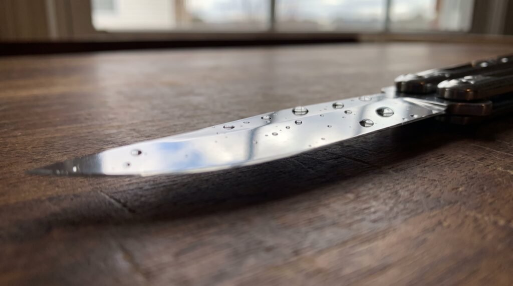 Macro of a mirror polished stainless butterfly knife blade with water droplets beading on the steel surface