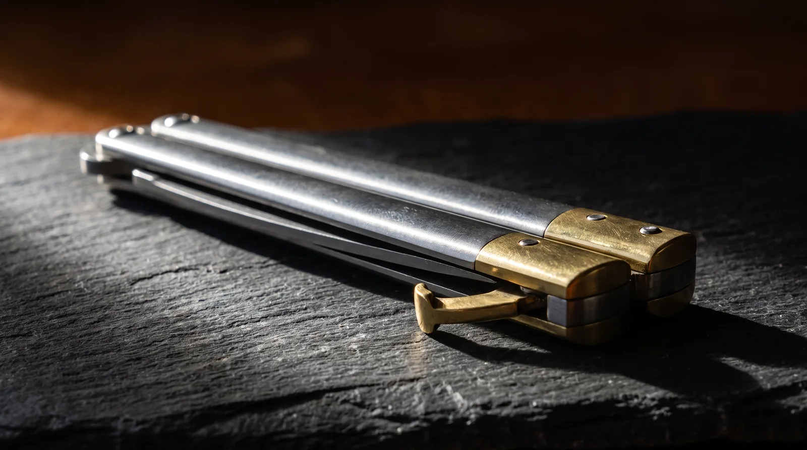 Closed butterfly knife on slate with its latch swung down against the brass bolster