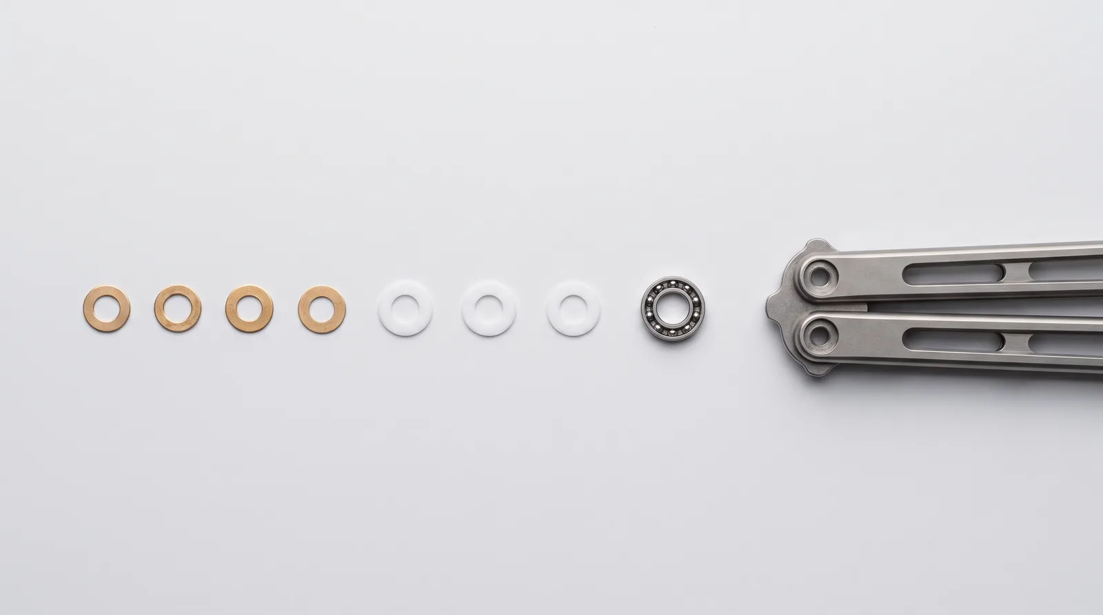Phosphor bronze washers, PTFE washers and a small bearing race laid out beside a balisong handle