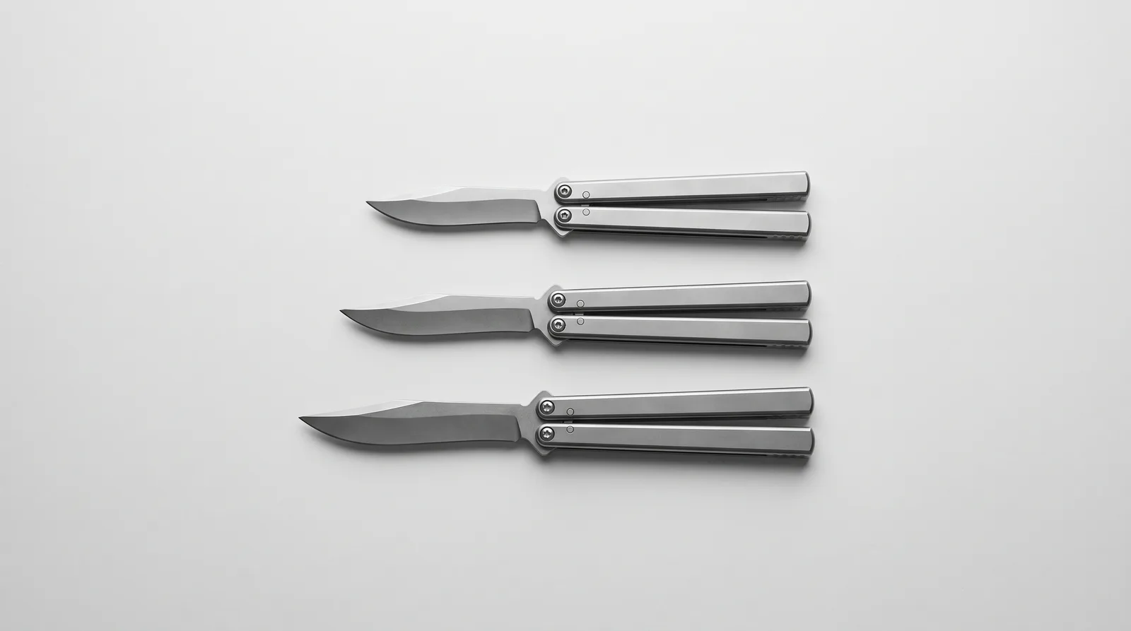 Three closed Batangas balisongs of clearly different lengths laid parallel on a grey background