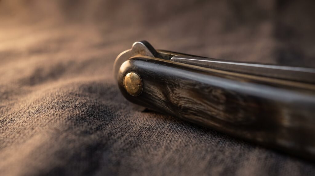 Macro view of the buffalo horn handle and brass pivot pin of a closed balisong butterfly knife resting on grey linen cloth