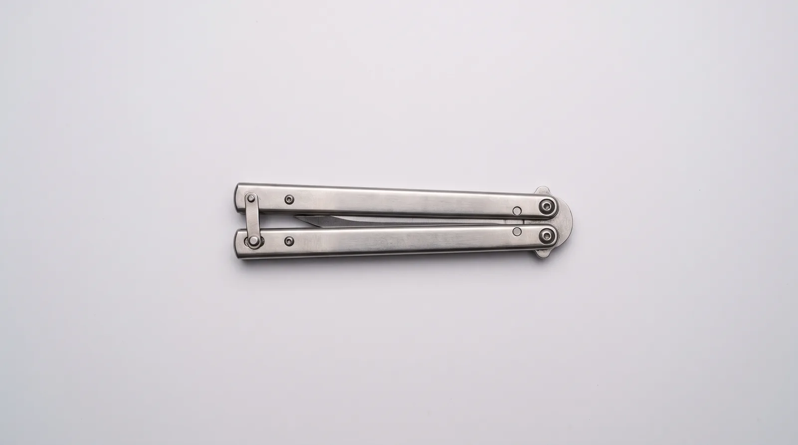 Butterfly knife lying closed on grey seamless with its latch resting against the opposite handle