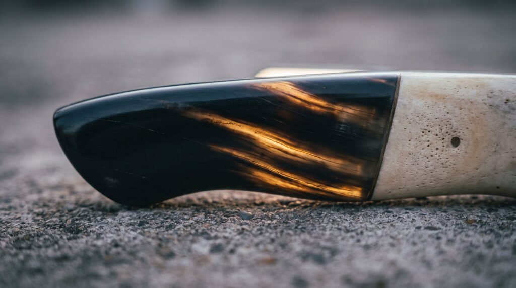 Macro of a polished knife handle block of black water buffalo horn joined to pale bone, backlight showing amber streaks in the horn