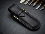 Handmade black full-grain leather balisong butterfly knife sheath with brass rivets, shown with hand tools