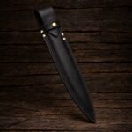 Black leather balisong chef knife sheath with hand stitched edges and brass rivets, standing upright