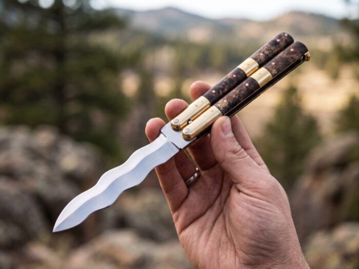 Habagat Pandayan balisong butterfly knife held open in hand outdoors showing the wavy blade edge