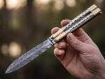 Monarch Filipino balisong butterfly knife held open in hand outdoors, brass and bone handle