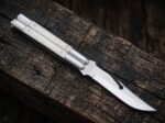 Moth balisong butterfly knife closed on a dark wood plank