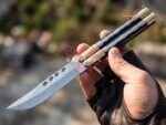 Mule Filipino balisong butterfly knife held open in a gloved hand, brass and kamagong wood handle